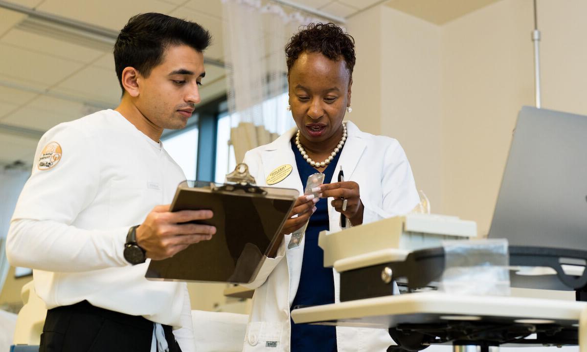 Two people on medical clothing look at a clipboard.